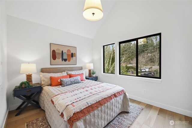 bedroom with light wood-type flooring and high vaulted ceiling