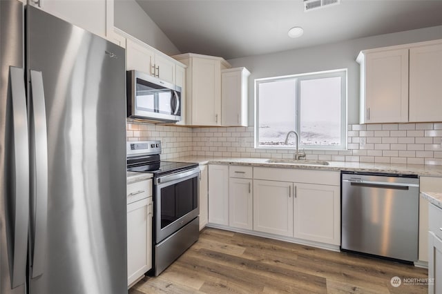 kitchen featuring sink, stainless steel appliances, wood-type flooring, light stone countertops, and white cabinets