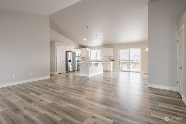 unfurnished living room featuring high vaulted ceiling, sink, and light hardwood / wood-style floors