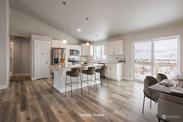 kitchen with decorative light fixtures, white cabinetry, decorative backsplash, a center island, and stainless steel appliances