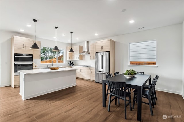 kitchen with gas cooktop, high end fridge, wall chimney exhaust hood, black double oven, and a kitchen island