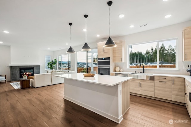 kitchen with sink, hanging light fixtures, black double oven, light wood-type flooring, and a kitchen island