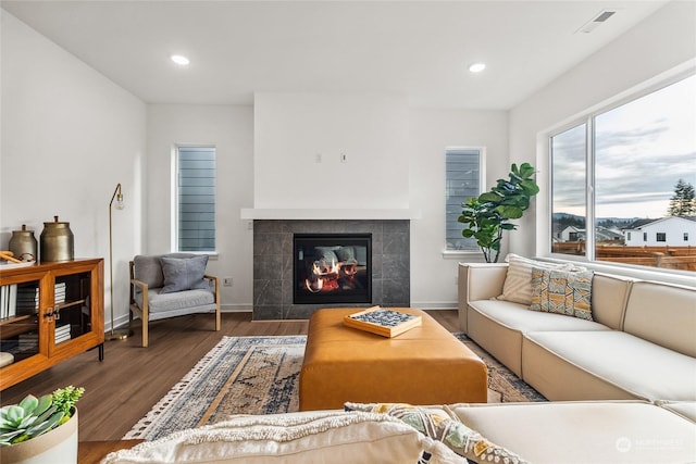 living room featuring a tiled fireplace and dark wood-type flooring