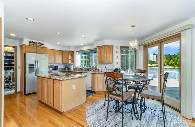 kitchen featuring light stone countertops, a center island, stainless steel appliances, hanging light fixtures, and light hardwood / wood-style floors