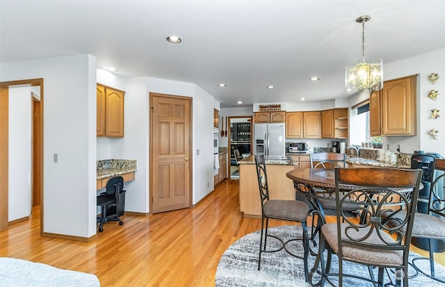 kitchen with appliances with stainless steel finishes, light wood-type flooring, light stone counters, a kitchen island, and hanging light fixtures