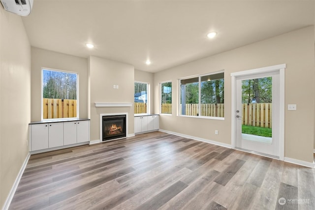 unfurnished living room featuring light wood-type flooring, a wealth of natural light, and an AC wall unit