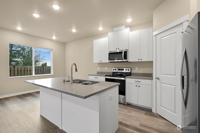 kitchen featuring appliances with stainless steel finishes, sink, light hardwood / wood-style flooring, white cabinetry, and an island with sink