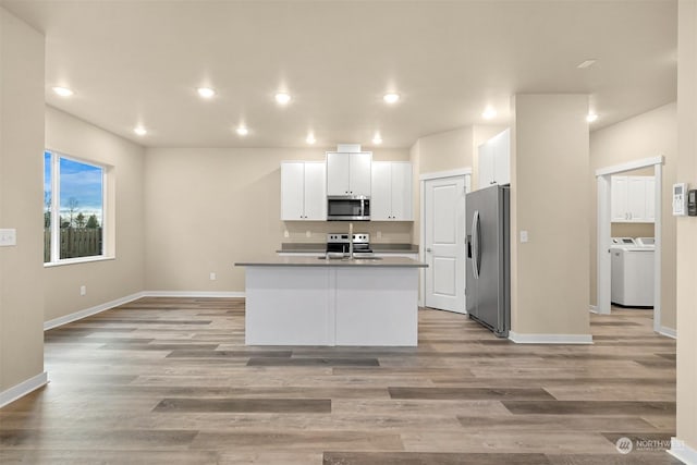 kitchen featuring white cabinets, light wood-type flooring, stainless steel appliances, and an island with sink