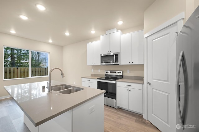 kitchen with white cabinets, sink, stainless steel appliances, and an island with sink