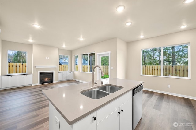 kitchen featuring stainless steel dishwasher, sink, wood-type flooring, a center island with sink, and white cabinetry