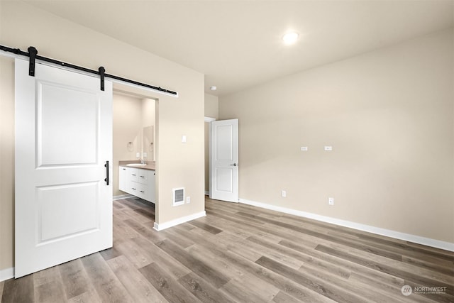 unfurnished bedroom featuring a barn door, ensuite bathroom, light hardwood / wood-style flooring, and sink