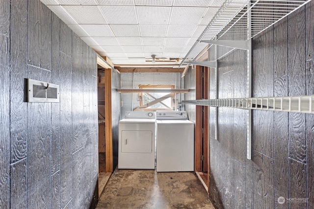 clothes washing area featuring washing machine and clothes dryer and wooden walls