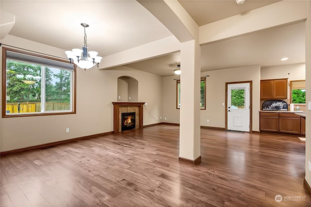 unfurnished living room with a tile fireplace, a healthy amount of sunlight, hardwood / wood-style floors, and an inviting chandelier