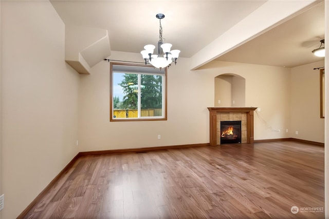 unfurnished living room with a chandelier, wood-type flooring, and a tiled fireplace