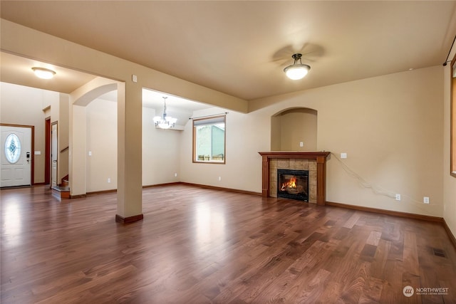 unfurnished living room featuring a tiled fireplace, dark wood-type flooring, and a chandelier