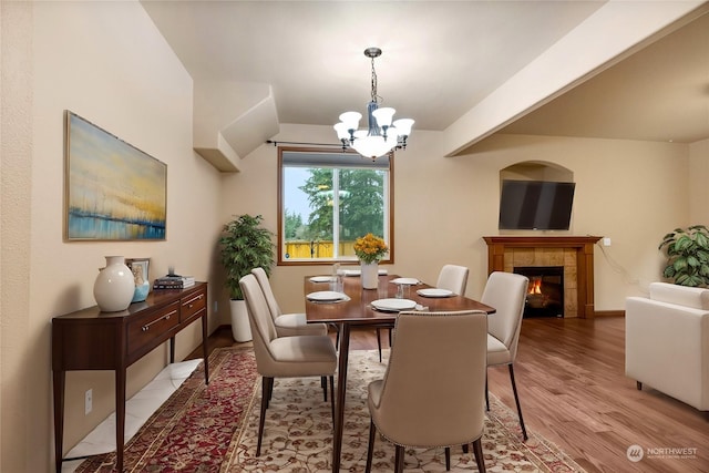 dining space featuring a tiled fireplace, a notable chandelier, and light hardwood / wood-style floors