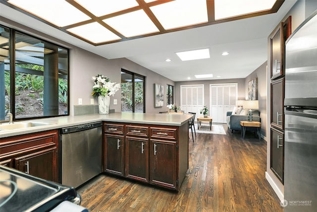 kitchen with sink, kitchen peninsula, dark brown cabinets, dark hardwood / wood-style floors, and appliances with stainless steel finishes