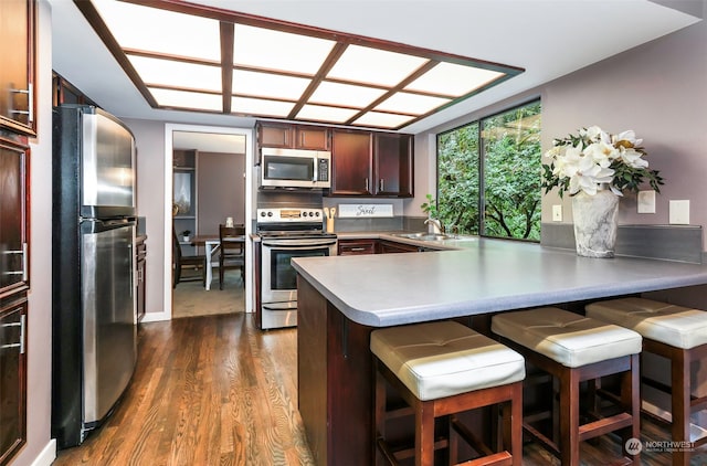 kitchen featuring stainless steel appliances, sink, a kitchen bar, kitchen peninsula, and dark wood-type flooring