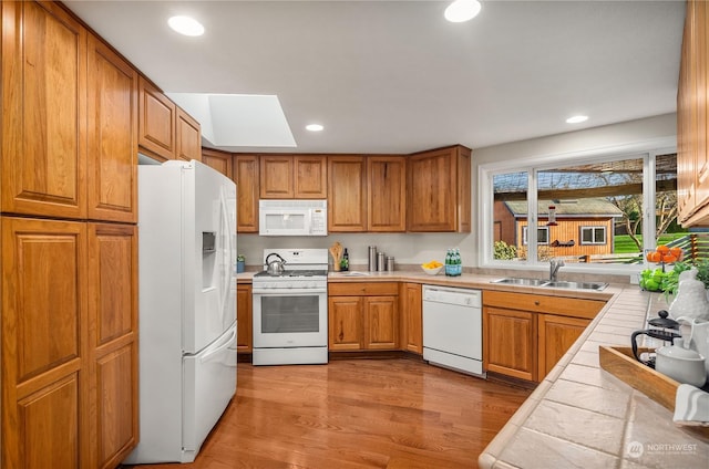 kitchen with sink, a skylight, light hardwood / wood-style flooring, tile counters, and white appliances