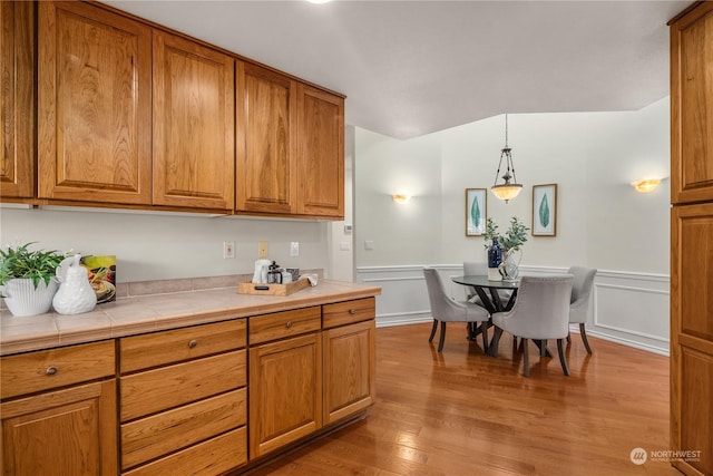 kitchen with hanging light fixtures, tile counters, and light hardwood / wood-style flooring