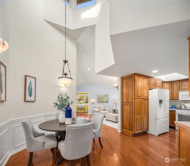 dining area with vaulted ceiling with skylight and light hardwood / wood-style floors