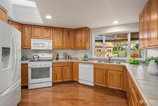 kitchen featuring sink, tile countertops, white appliances, and light hardwood / wood-style flooring