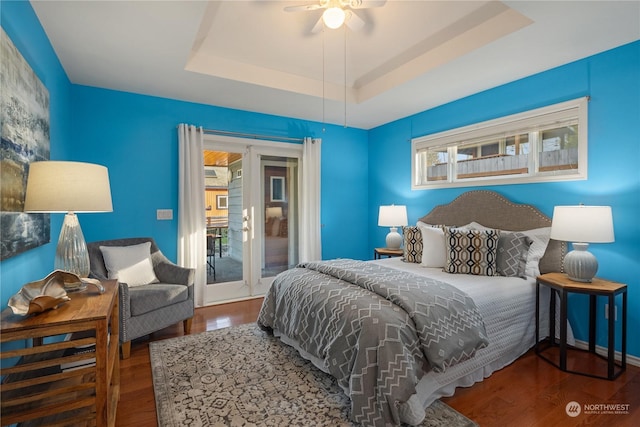 bedroom with hardwood / wood-style flooring, access to exterior, ceiling fan, a raised ceiling, and french doors