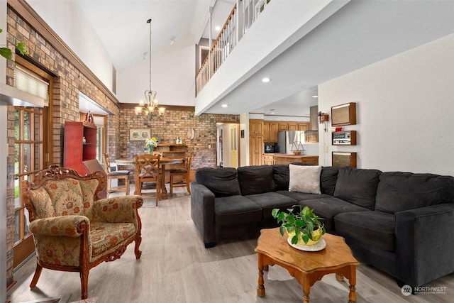 living room featuring a chandelier, light wood-type flooring, high vaulted ceiling, and brick wall