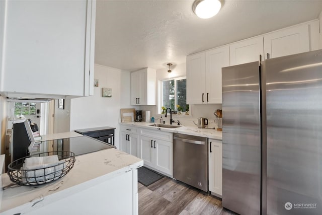 kitchen with appliances with stainless steel finishes, light wood-type flooring, a healthy amount of sunlight, sink, and white cabinetry