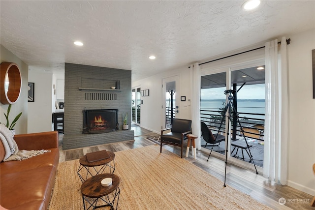 living room with a fireplace, light hardwood / wood-style floors, a water view, and a textured ceiling