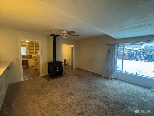 unfurnished living room with a wood stove, ceiling fan, carpet, and a textured ceiling