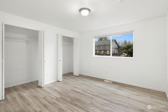 unfurnished bedroom featuring two closets and light hardwood / wood-style flooring