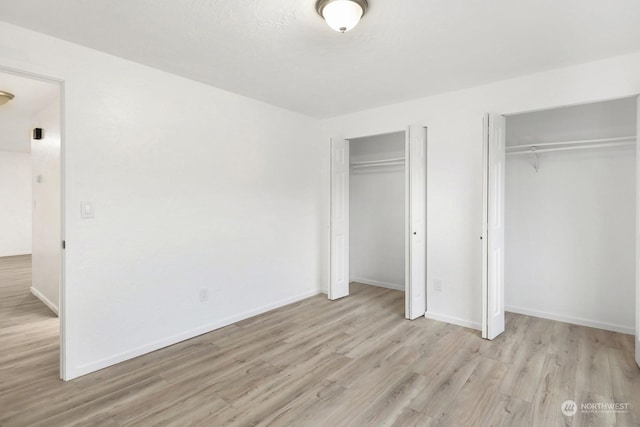 unfurnished bedroom with multiple closets and light wood-type flooring