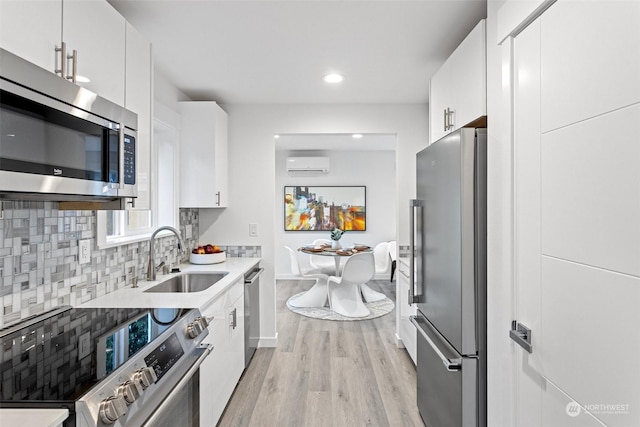 kitchen with appliances with stainless steel finishes, a wall mounted air conditioner, white cabinetry, sink, and backsplash