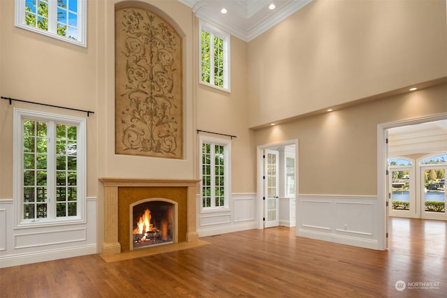 unfurnished living room featuring a fireplace, wood-type flooring, a towering ceiling, and crown molding