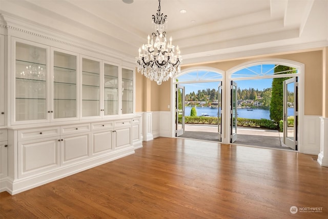 unfurnished dining area with a raised ceiling, a water view, hardwood / wood-style floors, and a chandelier