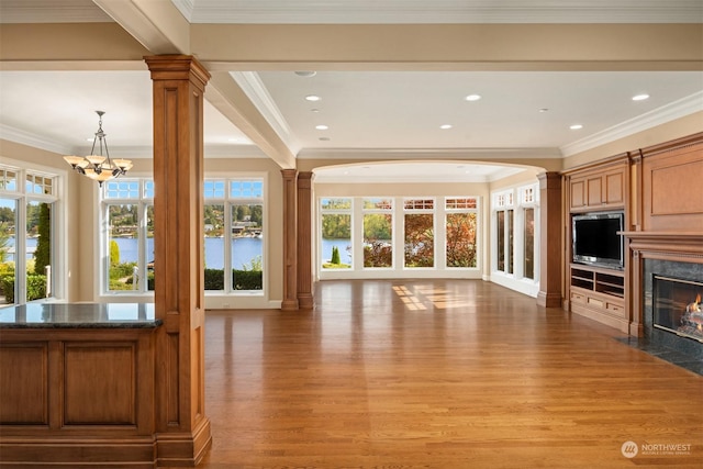 unfurnished living room featuring ornate columns, a notable chandelier, ornamental molding, and a premium fireplace