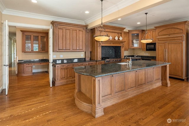 kitchen with a center island with sink, decorative light fixtures, crown molding, and hardwood / wood-style flooring