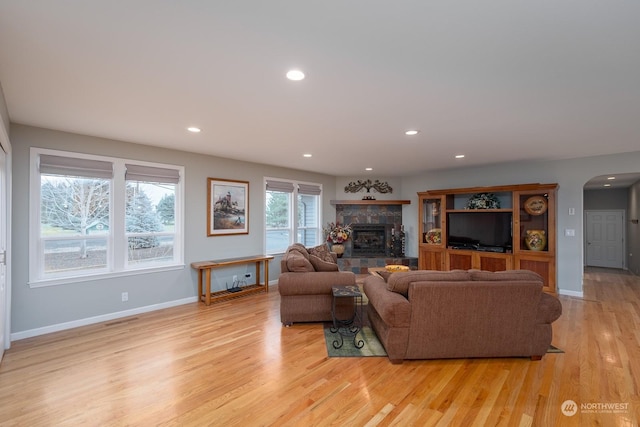 living room with a stone fireplace and light wood-type flooring