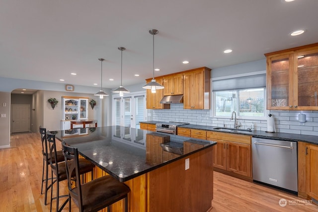 kitchen with backsplash, hanging light fixtures, appliances with stainless steel finishes, a kitchen island, and a kitchen bar