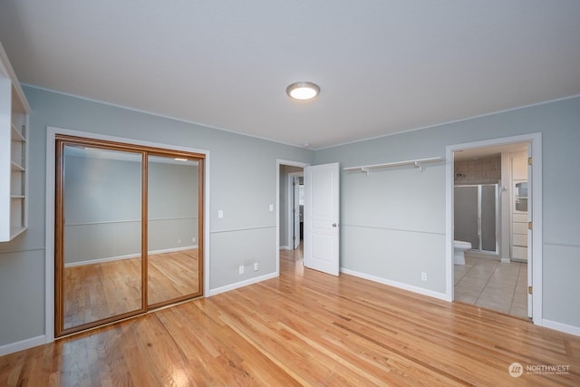 unfurnished bedroom featuring ensuite bath, a closet, and light wood-type flooring