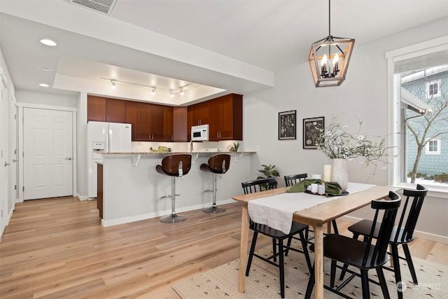 dining space with an inviting chandelier, track lighting, light hardwood / wood-style floors, and a raised ceiling