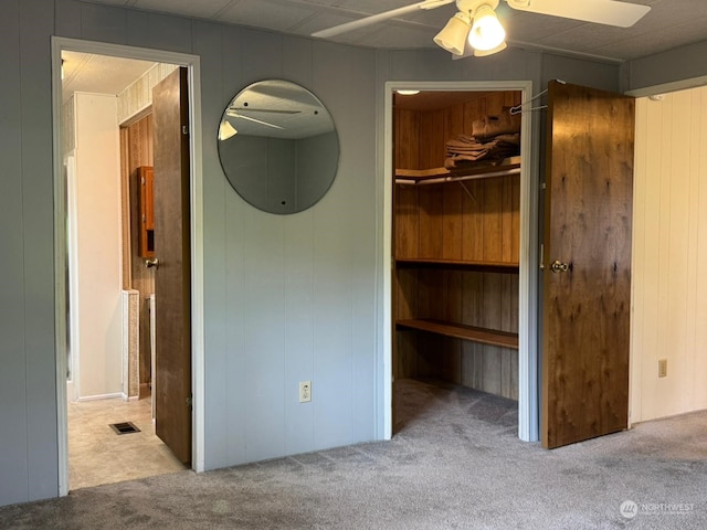 unfurnished bedroom with ceiling fan, light carpet, and wooden walls