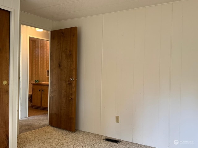 carpeted empty room featuring wood walls