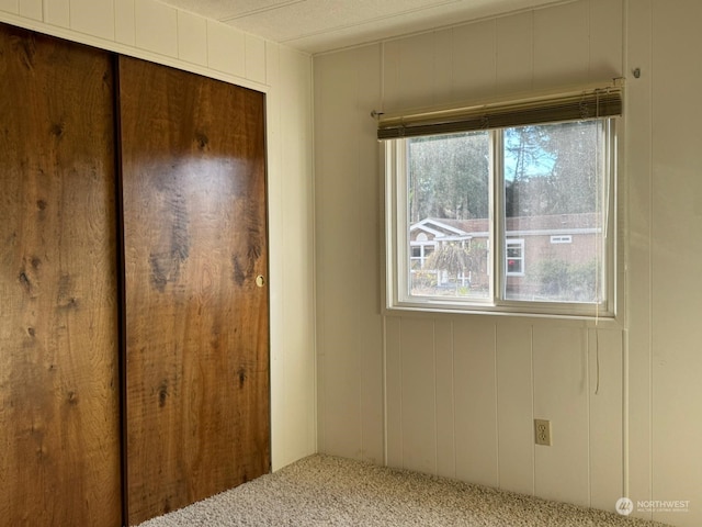 unfurnished bedroom featuring carpet flooring, multiple windows, wooden walls, and a closet