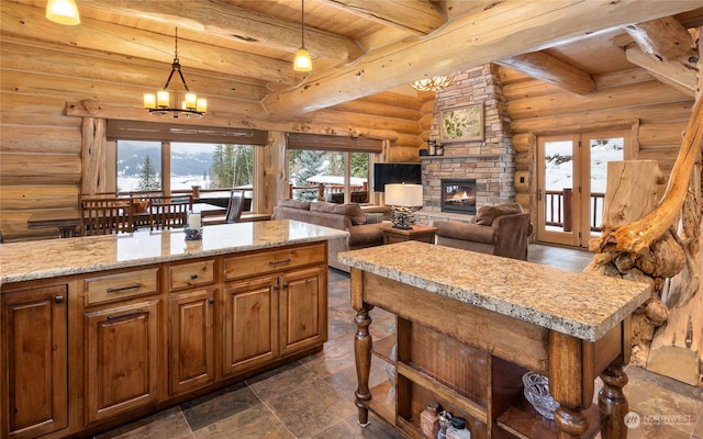 kitchen with a stone fireplace, rustic walls, decorative light fixtures, a kitchen island, and a notable chandelier