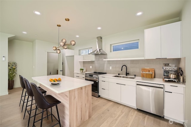 kitchen featuring pendant lighting, wall chimney range hood, sink, appliances with stainless steel finishes, and white cabinetry