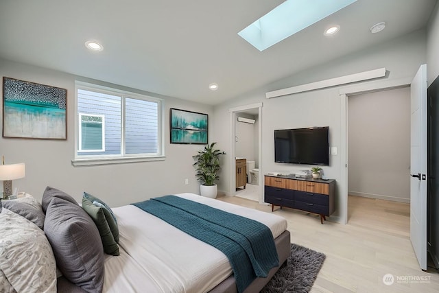 bedroom with vaulted ceiling with skylight, ensuite bathroom, a wall mounted AC, and light hardwood / wood-style flooring