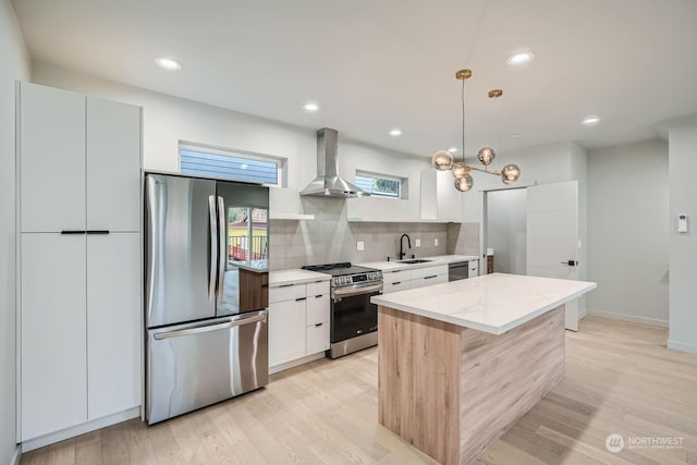 kitchen featuring appliances with stainless steel finishes, wall chimney exhaust hood, decorative light fixtures, white cabinetry, and a kitchen island