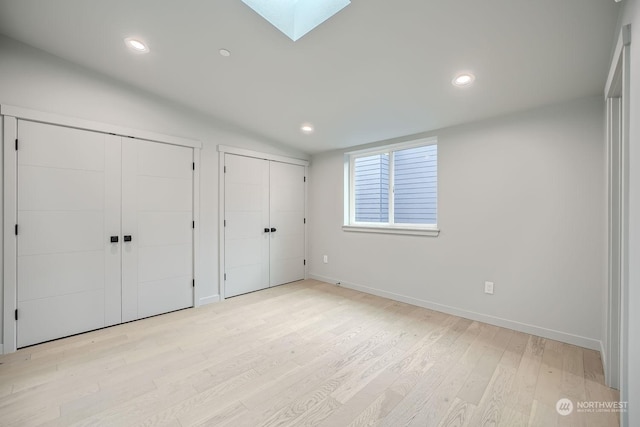 unfurnished bedroom featuring light hardwood / wood-style floors, lofted ceiling with skylight, and multiple closets